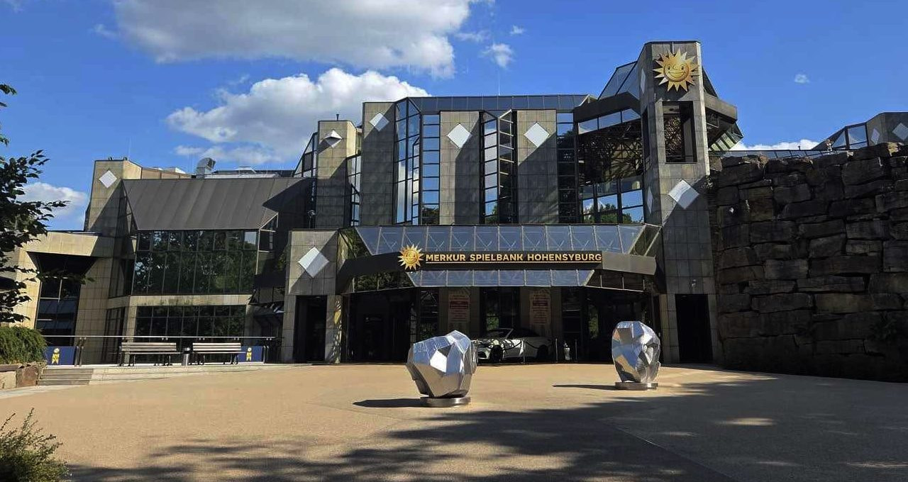 Eingang der MERKUR SPIELBANK Hohensyburg mit Glasfassade, Schriftzug und den Skulpturen auf dem Vorplatz